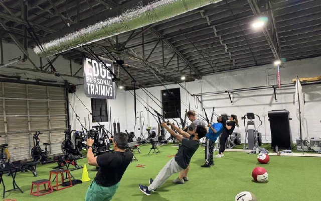 A small group of EDGE clients training with TRX suspension straps on the gym's turf floor